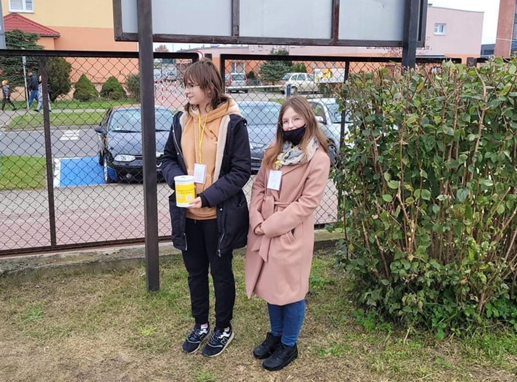 Grafika przedstawia uczennice SP 4 kwestujące na cmentarzu