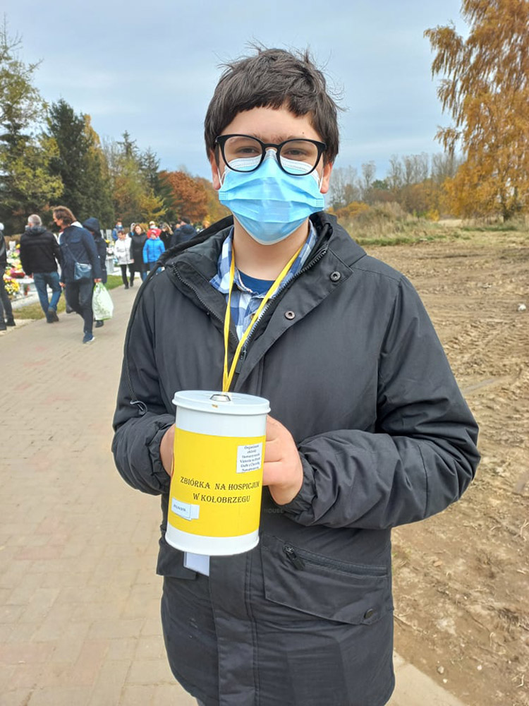 Grafika przedstawia ucznia SP4 podczas kwesty na rzecz na Hospicjum na cmentarzu Kołobrzeskim