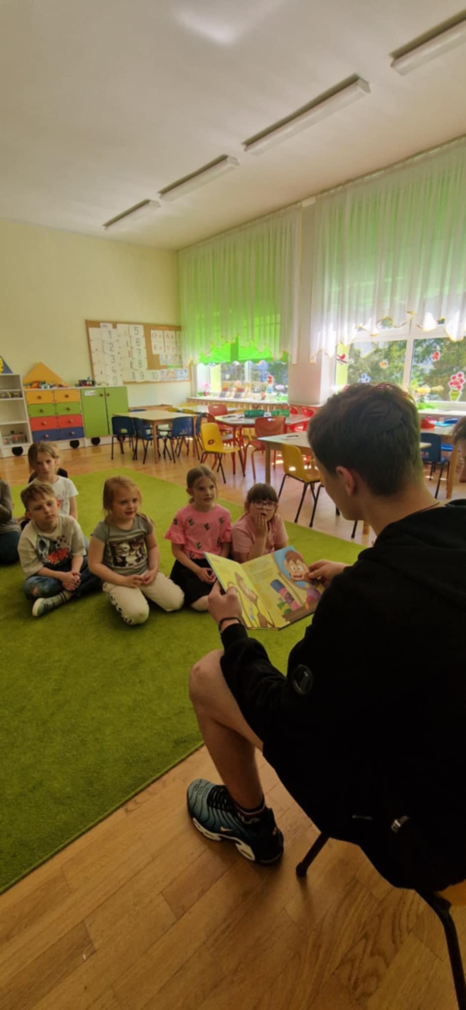 Chłopcy czytają książkę przedszkolakom.